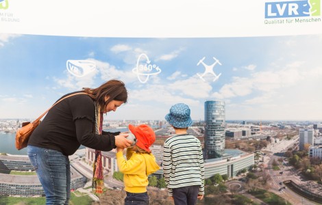 Frau und zwei Kinder, Mädchen mit VR-Brille vor Kölnpanorama