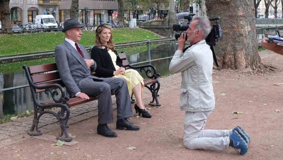 Kameramann kniet vor zwei Schauspielern auf einer Parkbank an einem Wassergraben.