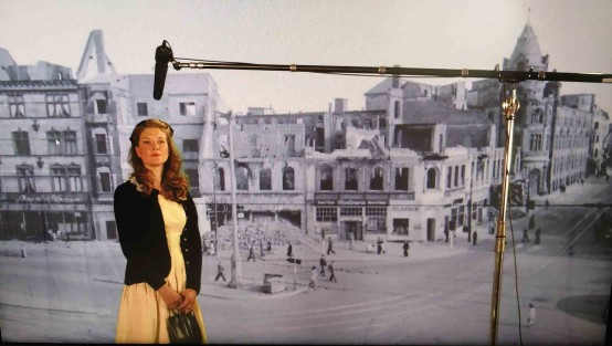 Schauspielerin  mit Ton-Angel vor einem schwarz-weiß-Foto mit Häuserruinen im Studio.