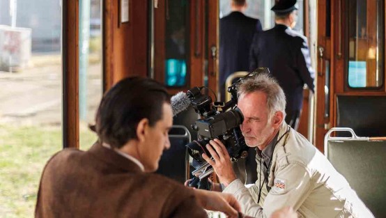 Schauspieler sitzt in einer historischen Straßenbahn und wird vom Kameramann gefilmt.