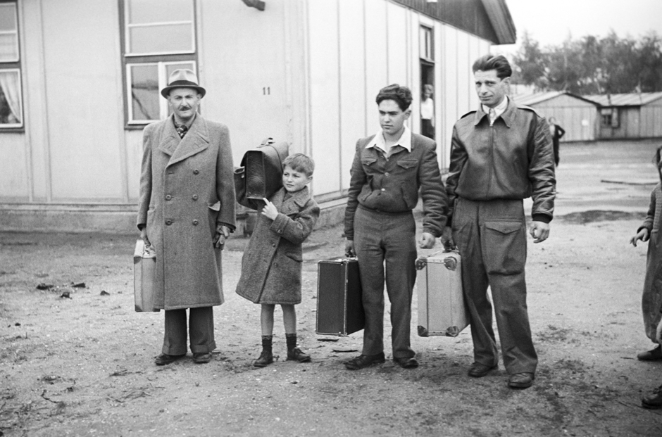 Zwei Männer und zwei Jungen stehen mit Koffern im Freien