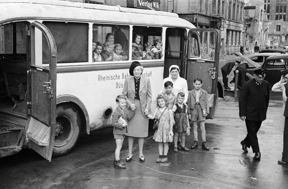 Fünf Kinder und zwei Betreuerinnen stehen vor einem Bus