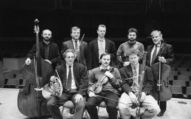 Acht Männer mit unterscheidlichen Instrumenten auf einer Konzerthausbühne