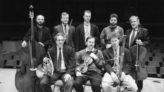 Acht Männer mit unterscheidlichen Instrumenten auf einer Konzerthausbühne