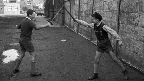 Zwei Jungen in kurzen Hosen  fechten mit Holzschwertern