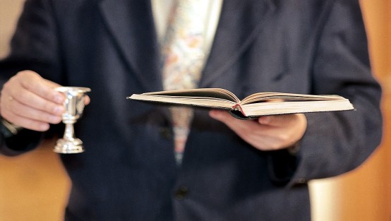 Ein Mann hält einen Kelch und ein aufgeschlagenes Buch in seinen Händen