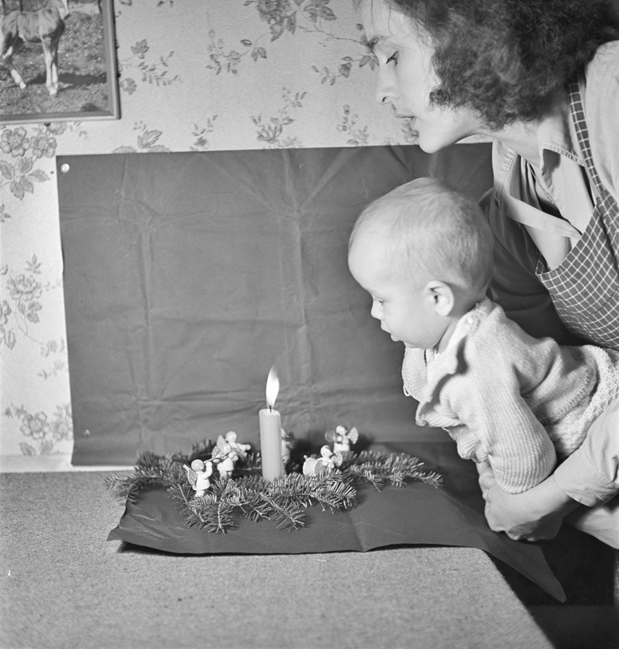 Eine Frau trägt ein Baby und steht neben einer Kerze.