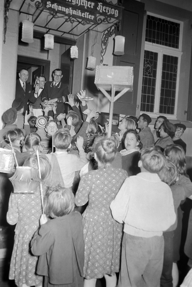 Kinder mit Laternen stehen vor einer Tür.