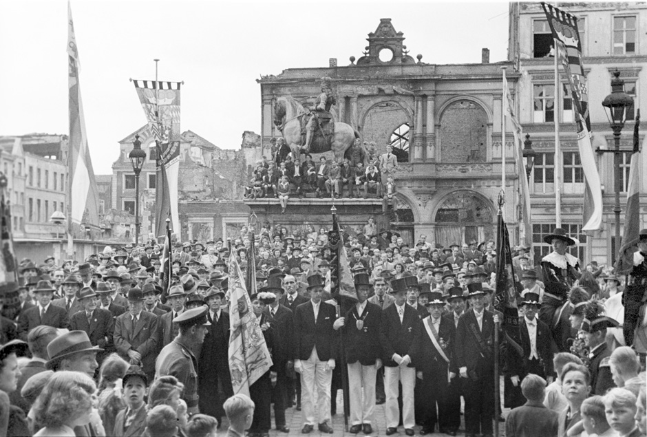 Menschen stehen auf einem Platz, der von Ruinen umgeben ist.