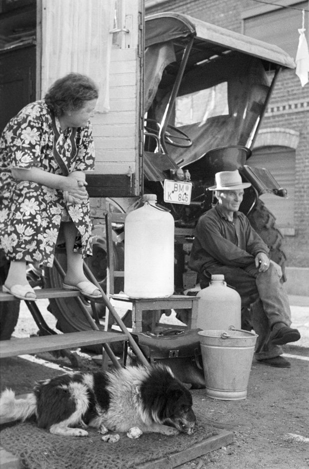 Eine Frau sitzt auf der Treppe eines Wohnwagens, vor der ein Hund liegt.