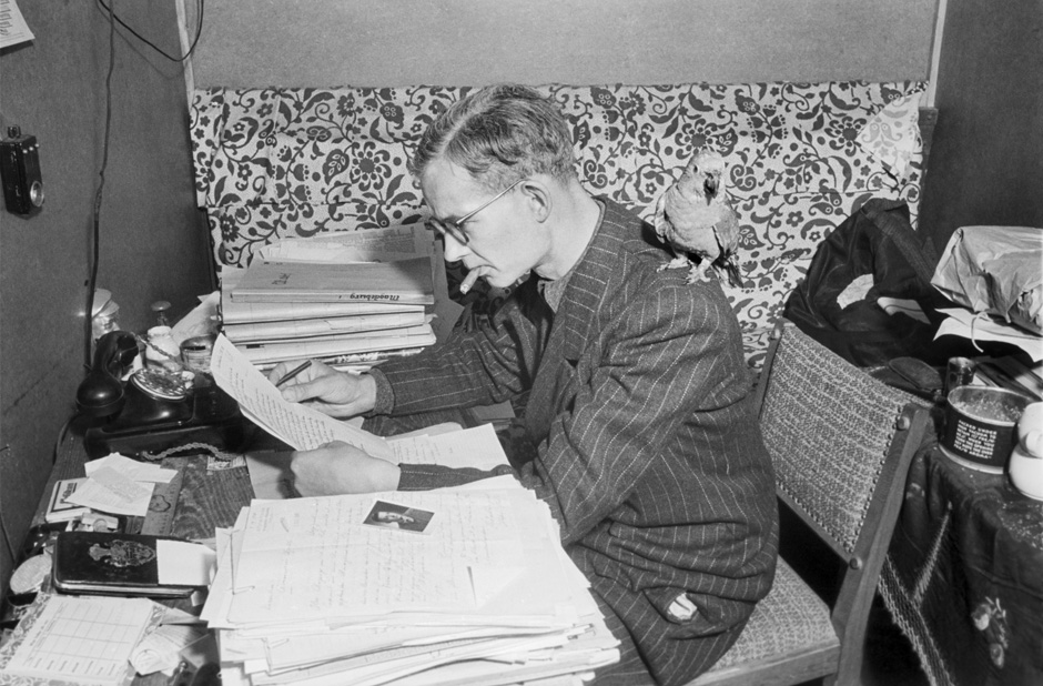 Ein Mann mit einem Vogel auf der Schulter sitzt an einem Schreibtisch.