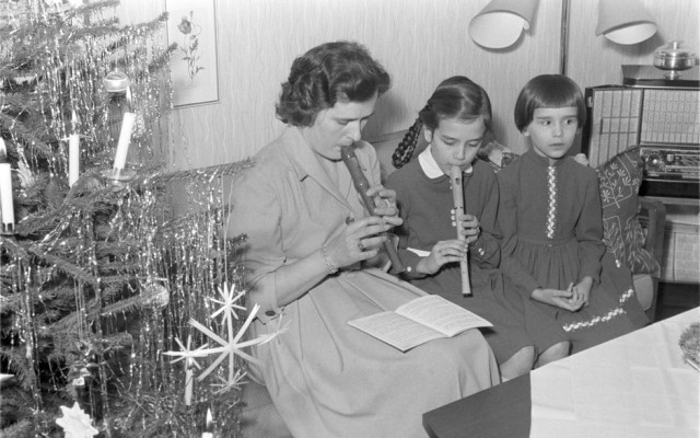 Eine Frau sitzt mit zwei Mädchen auf dem Sofa und spielt Flöte.