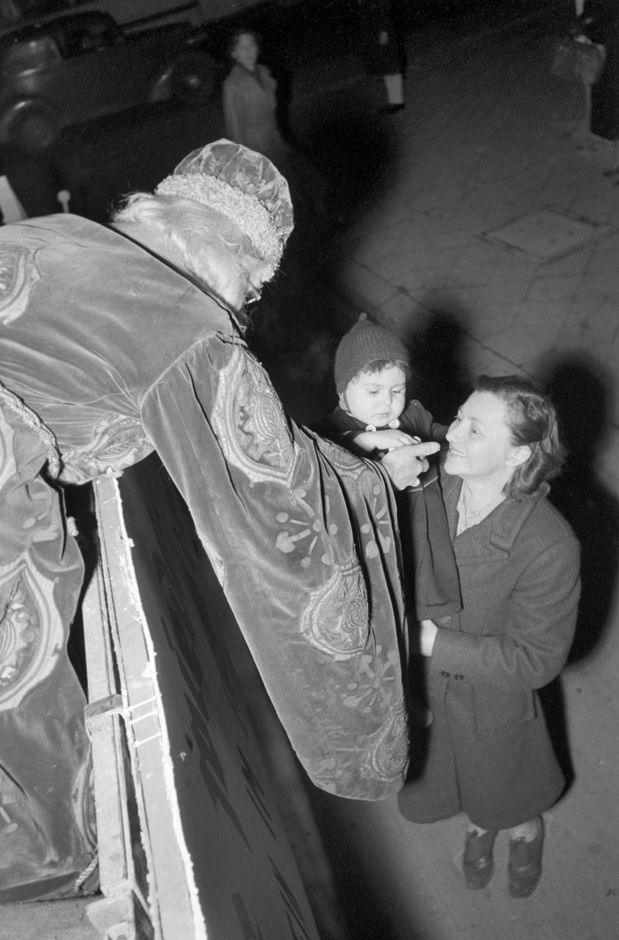 Der Nikolaus steht auf einem Wagen und reicht einem Kind Süßigkeiten.