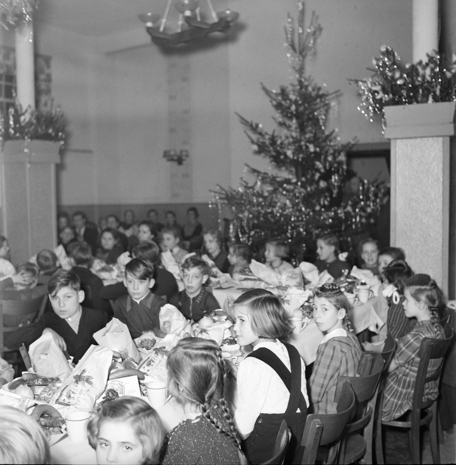 Kinder sitzen in einem Saal mit Weihnachtsbäumen.