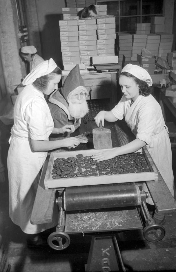 Der Nikolaus und zwei Frauen stehen neben einem Transportband.