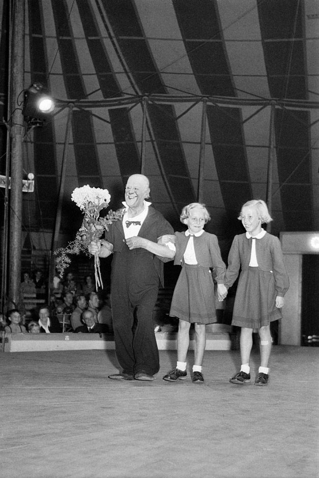 LVR-ZMB, C.A. Stachelscheid Ein Clown steht mit zwei Mädchen in einer Manege.
