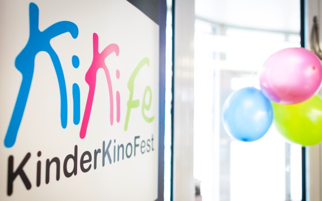 Links ist das Logo vom KiKiFe zu sehen, rechts einige Luftballons in den gleichen Farben: blau, magenta und grün.