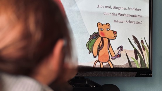 Auf der interaktiven Tafel ist ein Ausschnitt aus einem Buch zu sehen. Dort ist eine Löwin mit Rucksack illustriert. Darüber der Text: 