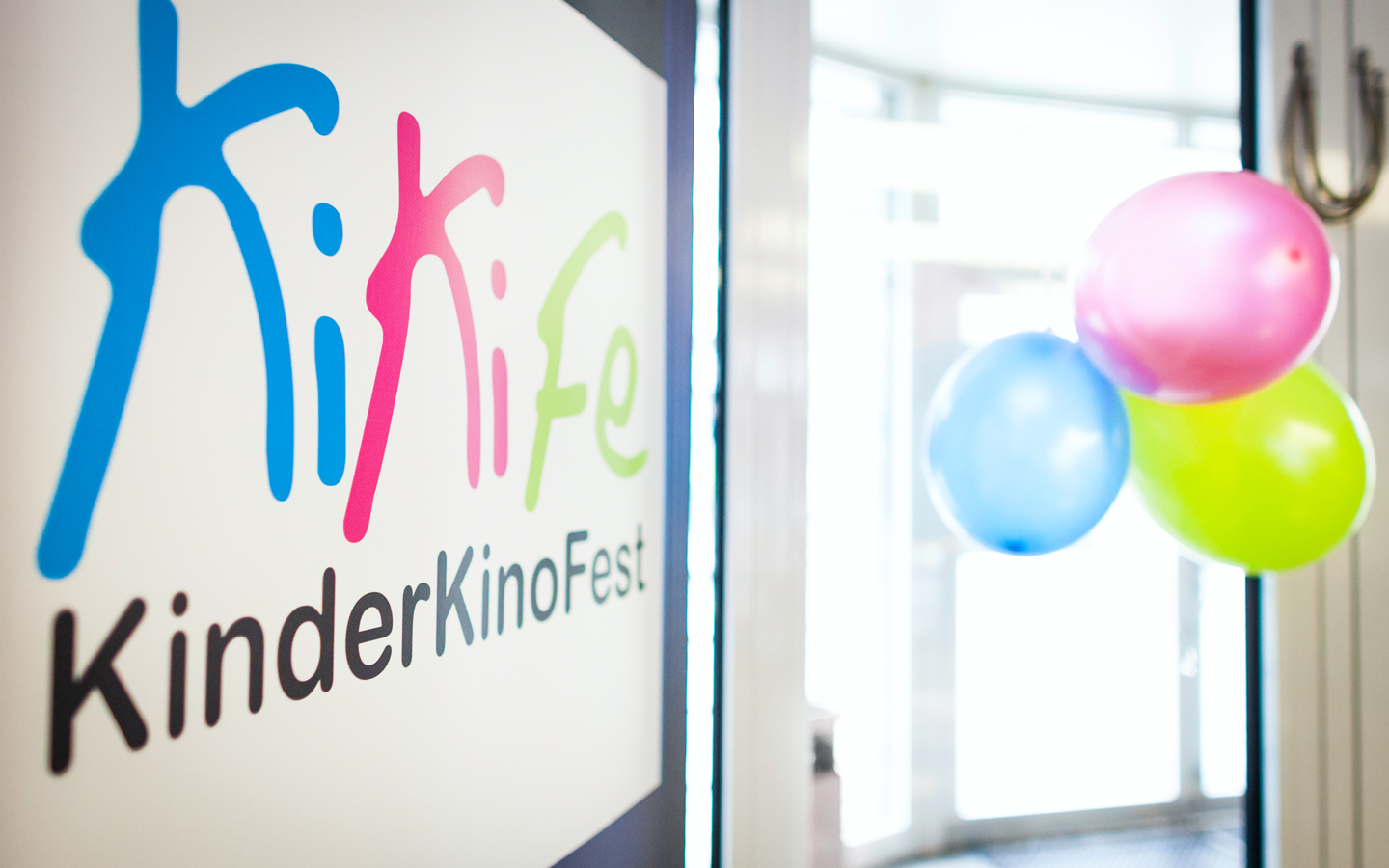 Links ist das Logo vom KiKiFe zu sehen, rechts einige Luftballons in den gleichen Farben: blau, magenta und grün.