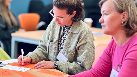 Zwei Fachkräfte lauschen gespannt dem Austausch in der Gruppe und notieren sich Stichpunkte auf Post-Its