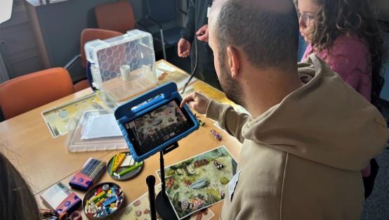  Fachkräfte arbeiten mit einem iPad auf einem Stativ, um mithilfe von kleinen Spielfiguren einen StopMotion-Film zu erstellen.
