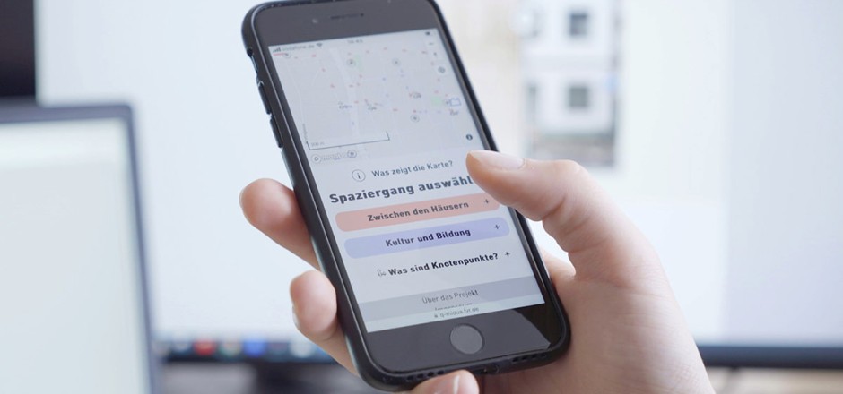 Eine Hand hält rein Handy mit der digitalen Stadtführung auf dem Bildschirm.