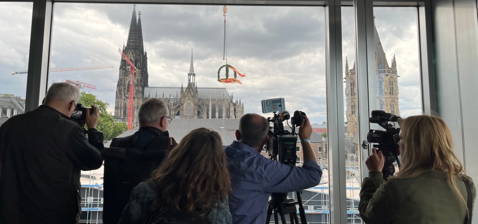 Presse und Kamerateam vor einem Fenster, draußen das Richtfest Richtfestaufnahmen