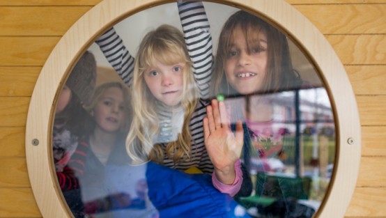 Vier Mädchen schauen durch ein rundes Fenster.