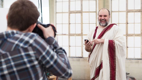 Fotograf fotografiert einen als Römer mit Tunika verkleideten Mann