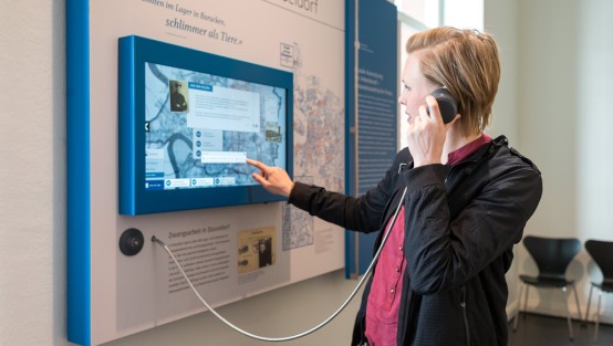 Besucherin am Touchscreen mit Hörer in der Hand