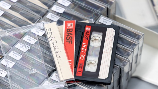 Eine Kiste mit Audiokassetten, darüber drei Kassetten die Kassettenbänder zeigen.