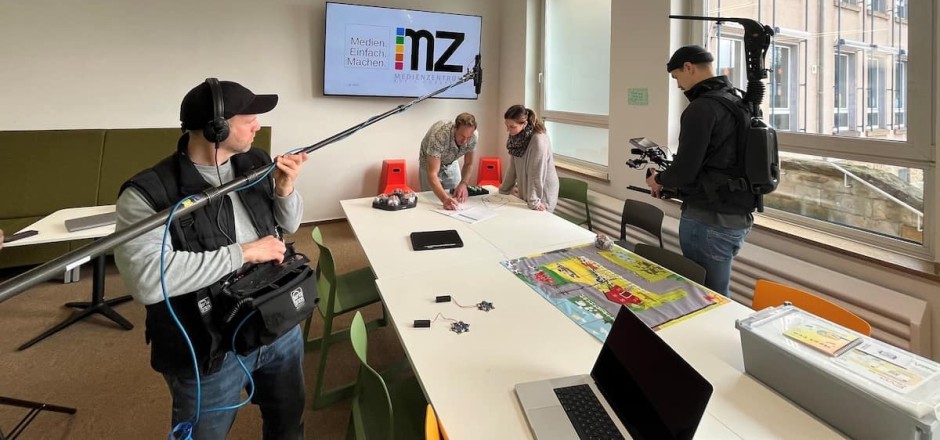 Kamerateam filmt eine Person die an einem Tisch steht.