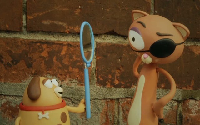 Zwei Spielzeugfiguren: Ein Hund hält der Katze mit einer Augenklappe einen kleinen Spiegel vors Gesicht.