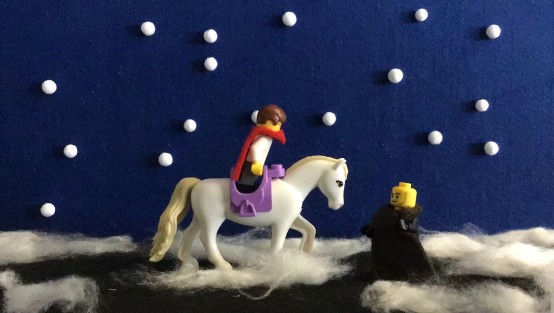 Zwei Lego-Figuren vor blauem Hintergrund mit Schneeflocken. Eine von ihnen sitzt auf einem weißen Pony.