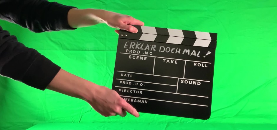 Filmklappe mit der Aufschrift "Erklär doch mal", vor grünem Hintergrund