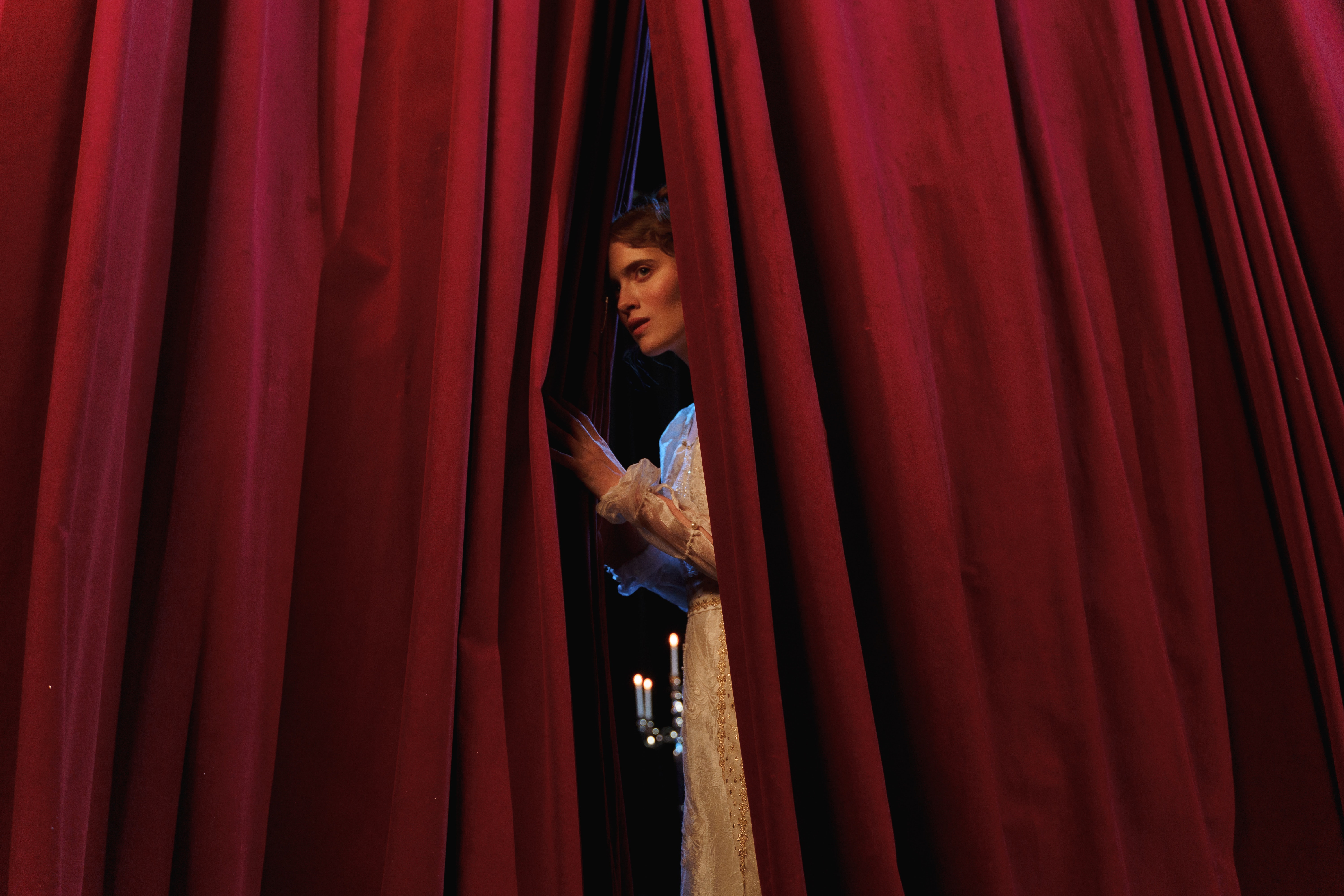 Frau blickt durch roten Vorhang