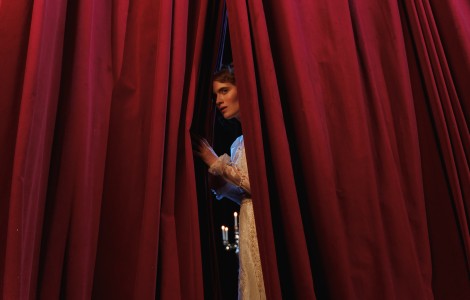 Frau steht zwischen rotem Vorhang.